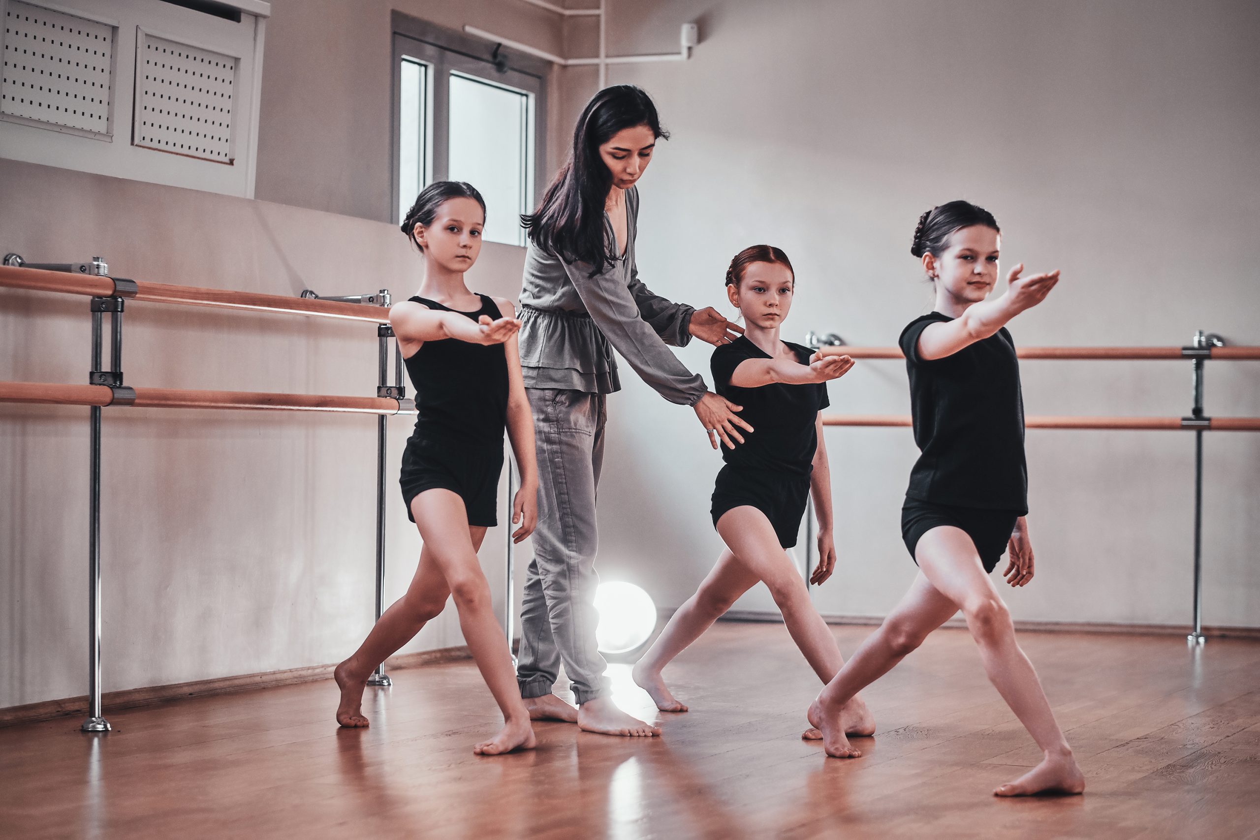 Three young girls have a ballet training with their attractive teacher
