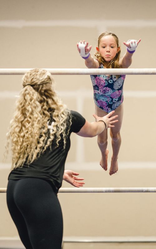 Overcoming Fear gymnast jumping to a bar with a coach guiding her