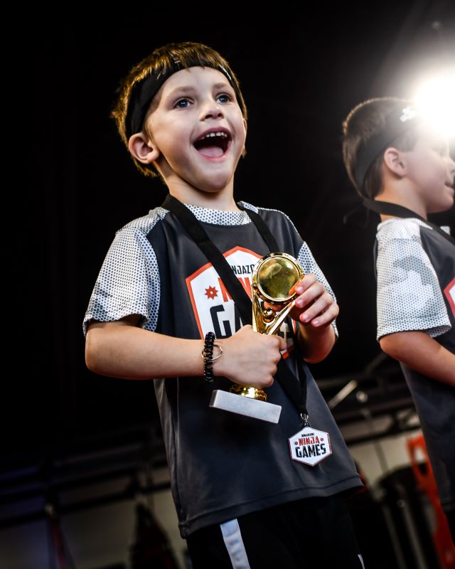 Lil ninja kid holding a trophy and smiling after winning